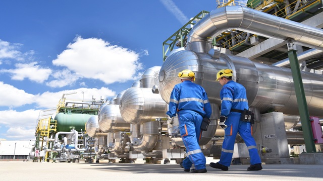Two mens in blue walking in front of a pretreatment biofuels system